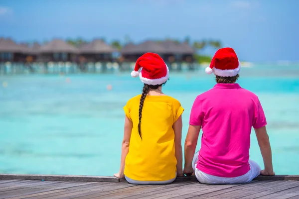 Back view of young couple in Santa hats on wooden jetty at Christmas vacation — Stock Photo, Image