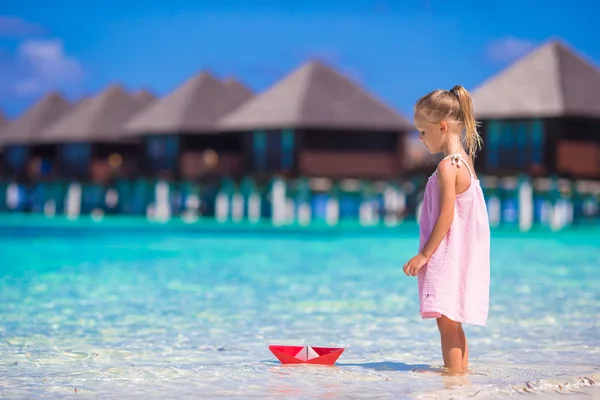Adorable little girl playing with origami boat in turquoise sea — Stock Photo, Image