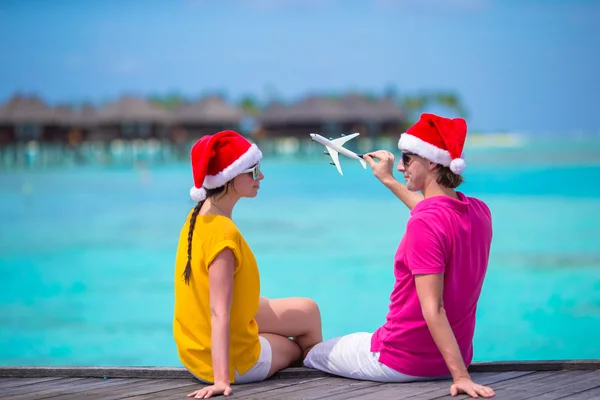 Mladý pár v Santa klobouky relaxační na dřevěné molo na vánoční prázdniny — Stock fotografie