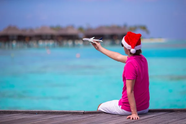 Mladý muž v santa hat během beach dovolenou na dřevěné molo s miniaturními letadla — Stock fotografie