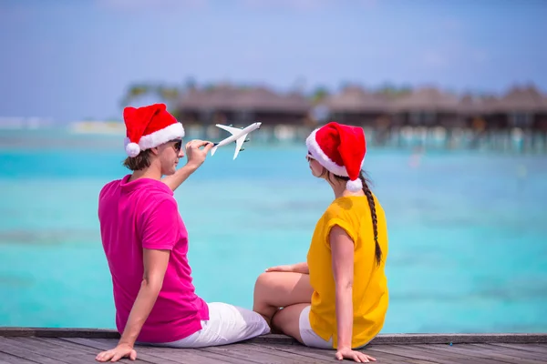 Mladý pár v Santa klobouky relaxační na dřevěné molo na vánoční prázdniny — Stock fotografie