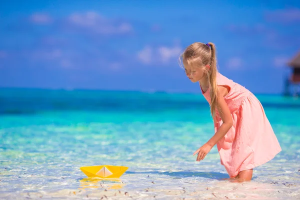 Adorable little girl playing with origami boat in turquoise sea — Stock Photo, Image