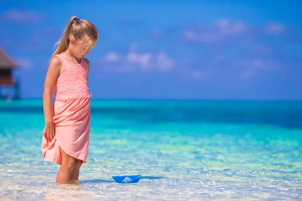 Adorable little girl playing with origami boat in turquoise sea — Stock Photo, Image