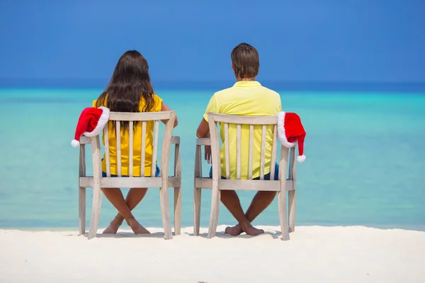 Rückansicht eines jungen Paares in Weihnachtsmützen, das es sich im Weihnachtsurlaub am tropischen Strand gemütlich macht — Stockfoto