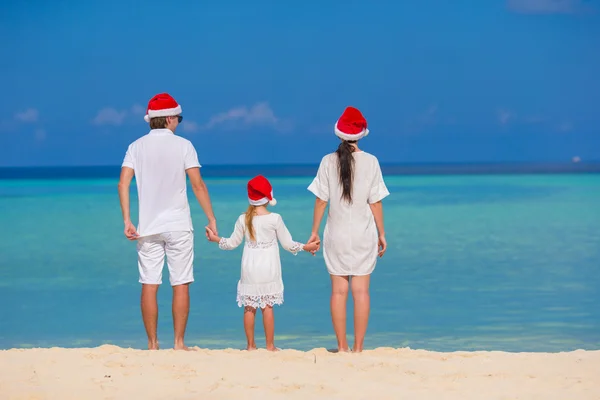 Gelukkig gezin van drie in Santa hoeden op strand — Stockfoto