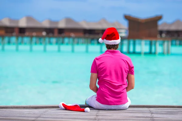 Giovane in cappello di Babbo Natale durante le vacanze al mare sul pontile di legno — Foto Stock
