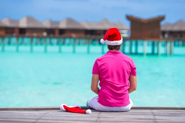 Mladý muž v santa hat během beach dovolenou na dřevěné molo — Stock fotografie