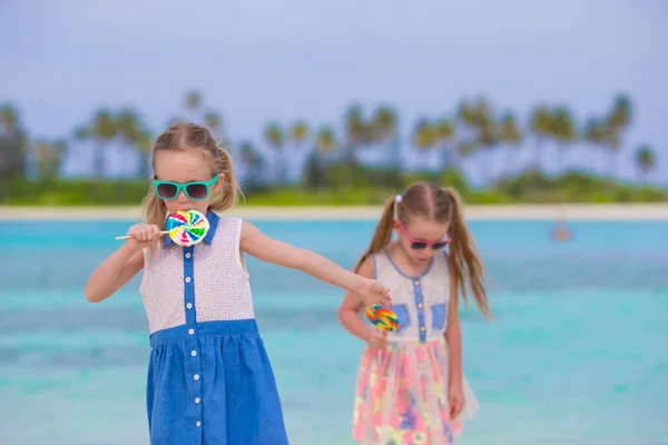 Two little girls with bright tasty lollipops on white beach — 图库照片