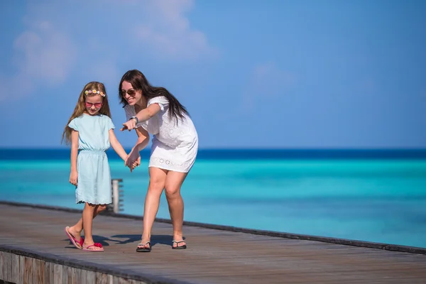 Niña y madre joven caminando en un embarcadero de madera en un resort exótico —  Fotos de Stock