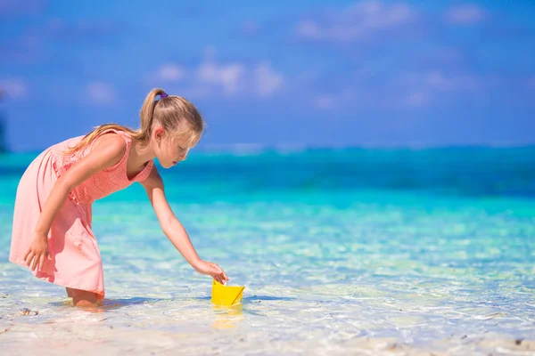 Adorable little girl playing with origami boat in turquoise sea — Stock Photo, Image