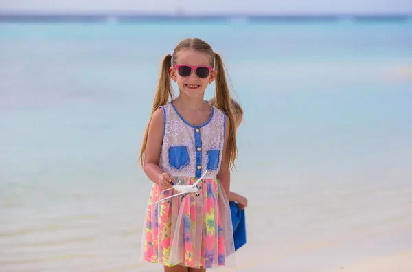 Happy little girl with toy airplane in hands on white sandy beach — Stock Photo, Image