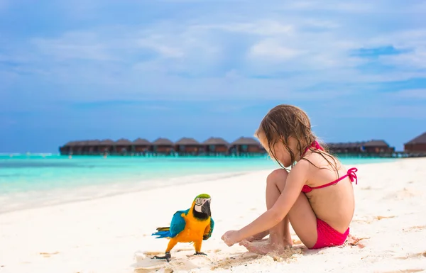 Adorable little girl at beach with big colorful parrot — Stock Photo, Image