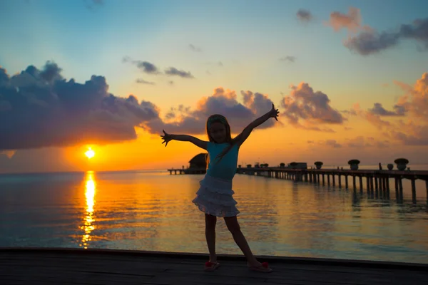 Silueta de adorable niña en embarcadero de madera al atardecer — Foto de Stock