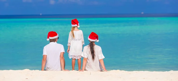 Glückliche dreiköpfige Familie mit Weihnachtsmützen am Strand — Stockfoto