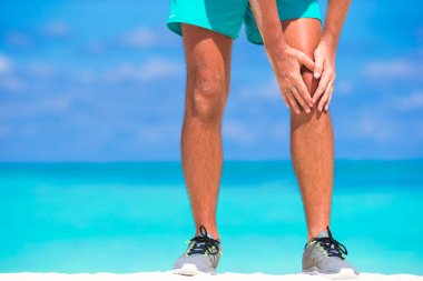 Beyaz kumsalda egzersiz yaparken bacak ağrısı muzdarip erkek atlet