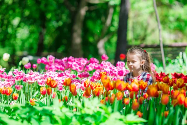 Kleines entzückendes Mädchen, das bunte Tulpen im Sommergarten riecht — Stockfoto