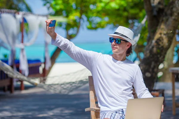 若い男は、熱帯のビーチでの携帯電話の写真を作る — ストック写真