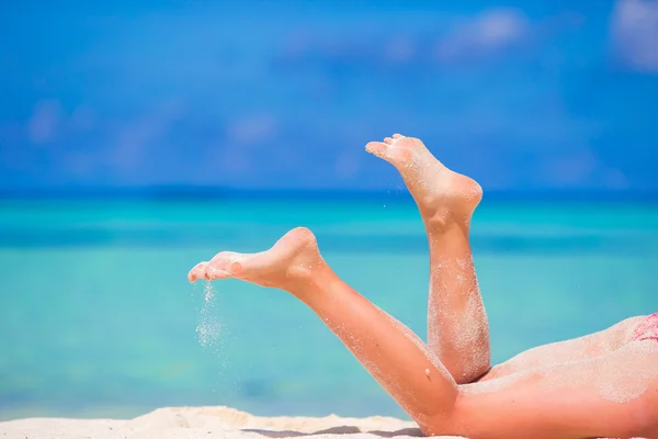 Womans beautiful slim tanned legs on white beach — Stock Photo, Image