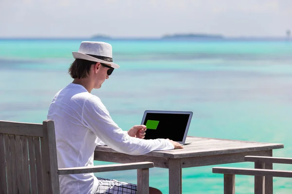 Young man working on laptop with credit card during tropical vacation — Stock Photo, Image