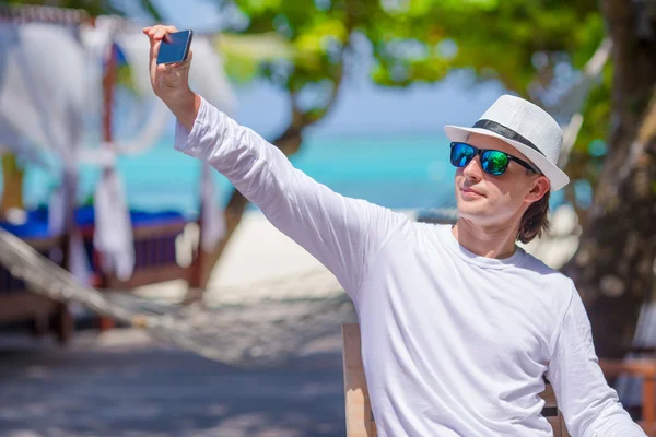 Ung man göra ett foto på mobiltelefon på tropical beach — Stockfoto