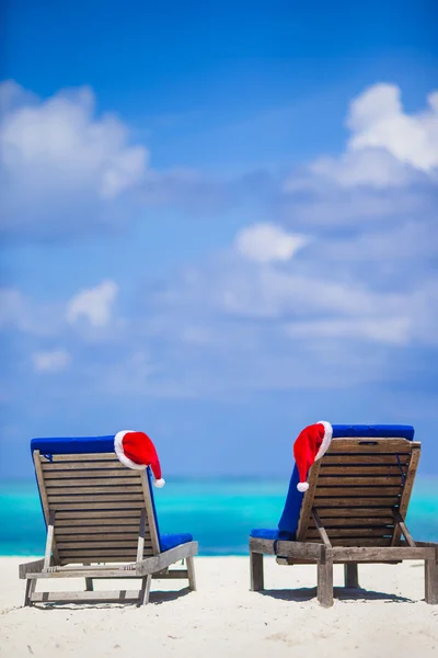 白い砂とターコイズ ブルーの水と熱帯のビーチでの赤いサンタ帽子と 2 つのラウンジ — ストック写真