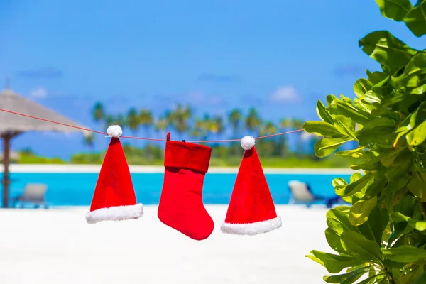 Červený Santa klobouky a Vánoční punčocha na tropické pláži — Stock fotografie