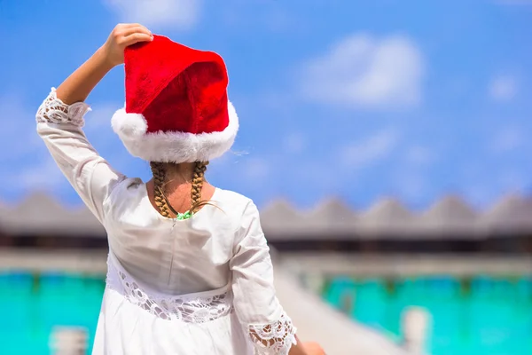 Kleines entzückendes Mädchen mit rotem Weihnachtsmann-Hut am Strand — Stockfoto