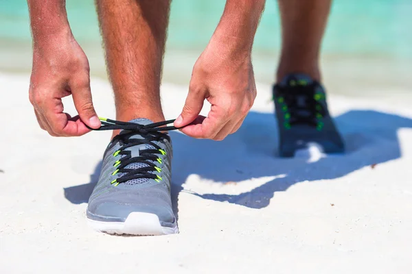 Running man tying running shoe laces on white beach
