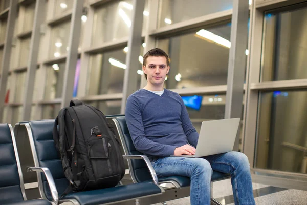 Молодой человек с ноутбуком и рюкзаком в аэропорту — стоковое фото