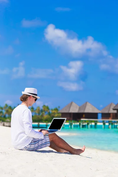 Anak muda bekerja pada laptop di pantai tropis dekat vila air — Stok Foto