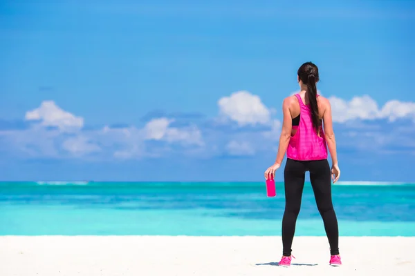 Fitte junge Frau trinkt Wasser am weißen Strand — Stockfoto