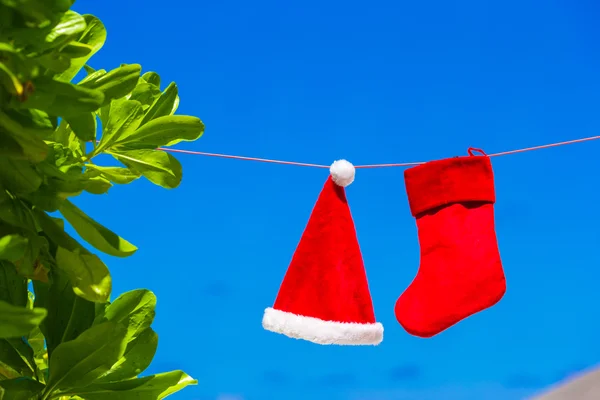 Topi Red Santa dan kaus kaki Natal tergantung di pantai tropis. Konsep Natal . — Stok Foto