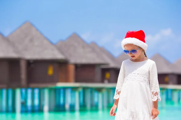 Pequena menina adorável em chapéu vermelho de Papai Noel na praia — Fotografia de Stock