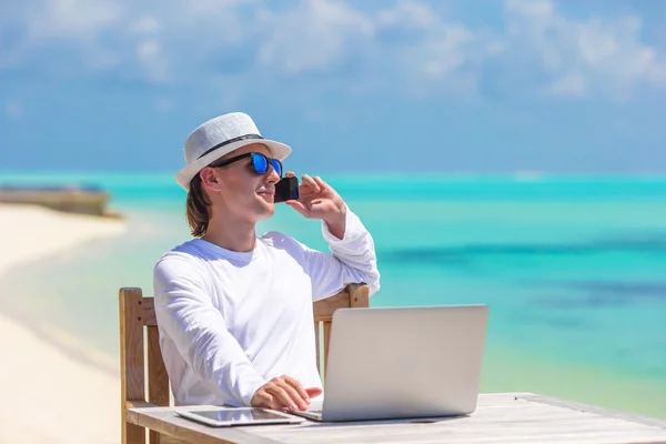 Young businessman with computer and cell phone on white beach — Stock Photo, Image