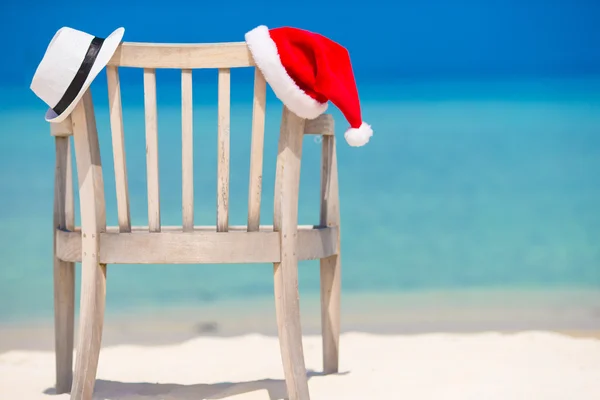 Red santa hat and white straw hat on beach chair at tropical vacation — Stock Photo, Image