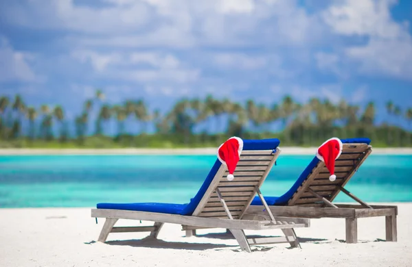 Két nyugágyat, piros Santa kalap a tropical beach fehér homokos és türkizkék vízzel — Stock Fotó