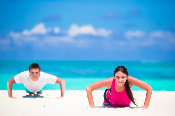 Jovem casal fitness fazendo flexões durante o treino de cross-training ao ar livre na praia tropical — Fotografia de Stock