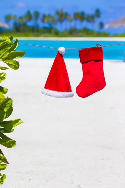 Red Santa hat and Christmas stocking hanging on tropical beach. Christmas concept. — Stock Photo, Image