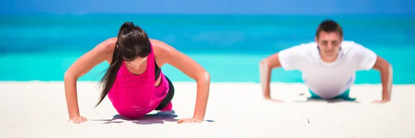 Joven pareja de fitness haciendo flexiones durante el entrenamiento cruzado al aire libre en la playa tropical —  Fotos de Stock