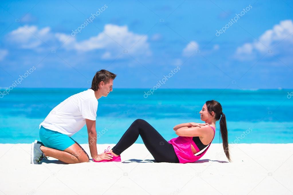 Young fitness couple doing side crunches on white beach during vacation