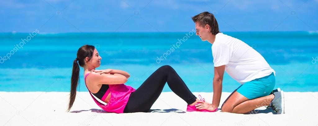 Young fitness couple doing side crunches on white beach during vacation
