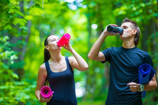 Jogging coppia attiva hanno un riposo con stuoia e bottiglia d'acqua all'aperto nella foresta — Foto Stock