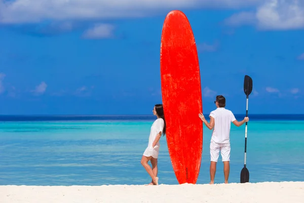 Young couple with red surfboard on white beach — Stock Photo, Image