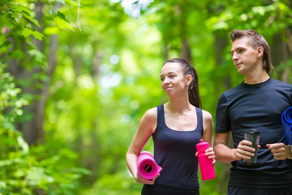 Jogging coppia attiva hanno un riposo con stuoia e bottiglia d'acqua all'aperto nella foresta — Foto Stock