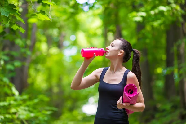 Young active fitness woman with mat and bottle of water outdoors — Stock Photo, Image