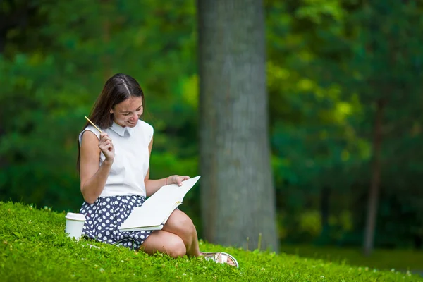 Junges Mädchen schreibt draußen im Park in ihr Notizbuch — Stockfoto