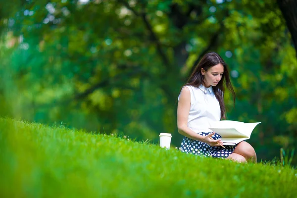 Jovem relaxante com café no parque lendo um livro — Fotografia de Stock