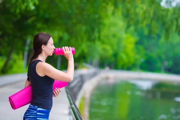 Молодая активная фитнес-женщина с ковриком и бутылкой воды на открытом воздухе — стоковое фото
