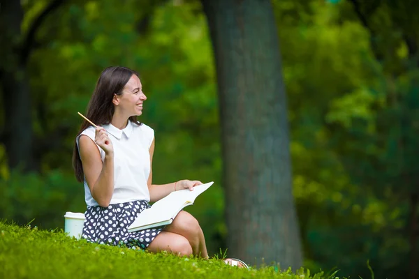 Młoda dziewczyna pisze w swoim notesie poza w parku — Zdjęcie stockowe