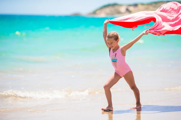 Милая маленькая девочка весело бегает с полотенцем на тропическом пляже с белым песком и бирюзовой водой океана — стоковое фото